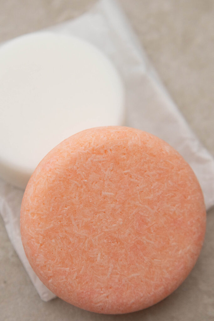 Two round solid shampoo bars, one orange and one white, on a neutral background. Eco-friendly hair care.