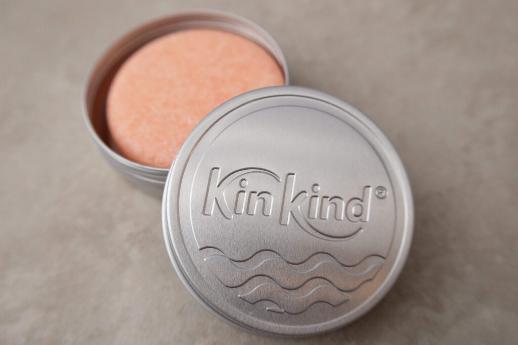 Pink shampoo bar inside a silver KinKind tin on a light surface, eco-friendly hair care product.