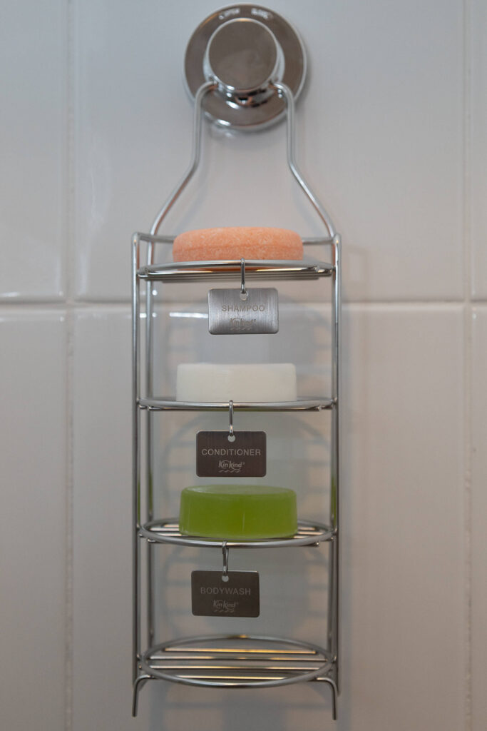 Triple-decker shower caddy with shampoo, conditioner, and bodywash bars on a tiled bathroom wall.