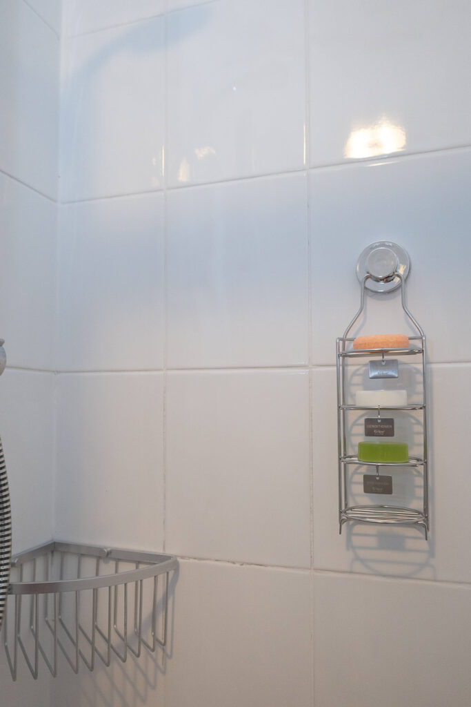 Shower caddy with soap bars and metal basket on white tiled bathroom wall.