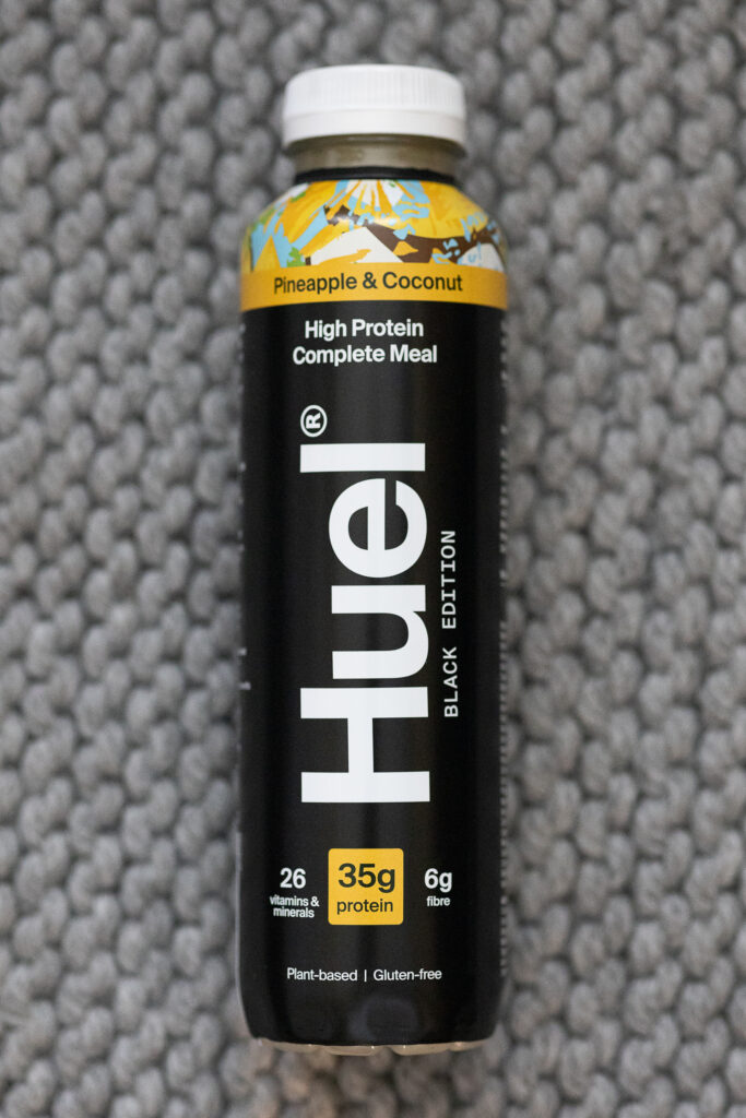 Huel Black Edition Pineapple & Coconut complete meal, 35g protein, plant-based, gluten-free drink on grey surface.