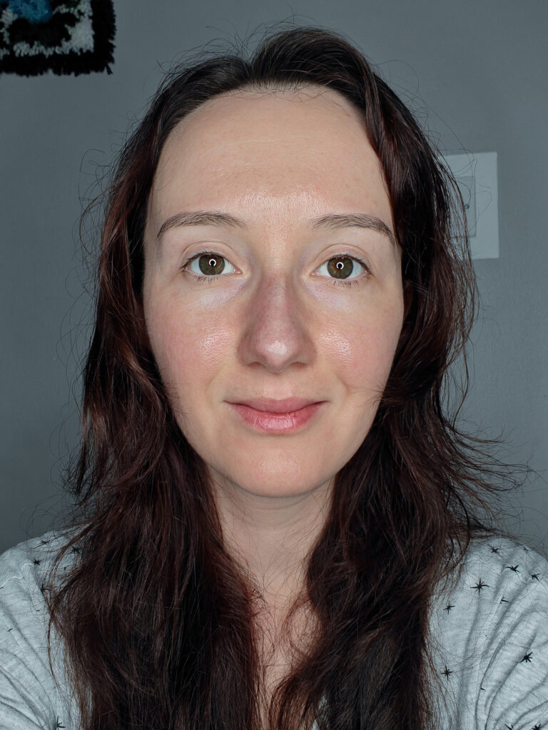 Portrait of a woman with long, dark hair and neutral expression against a grey background.
