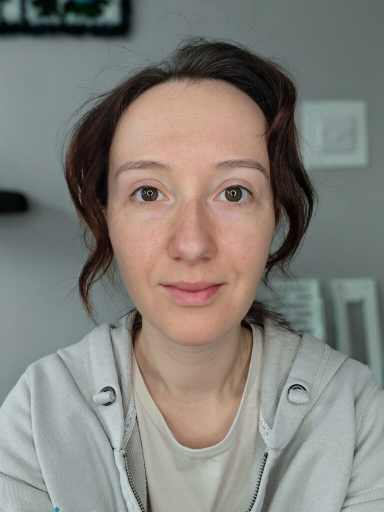 Person wearing a grey hoodie, looking directly at the camera with a neutral expression in a softly lit room.