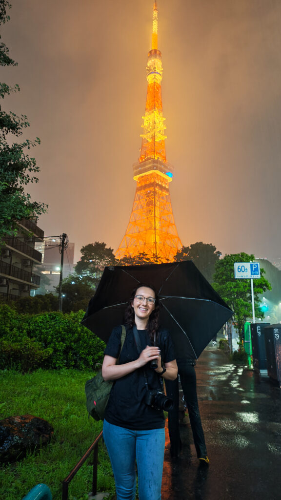 Japan travel tips - Smiling woman with umbrella in front of Tokyo Tower illuminated at night in the rain.