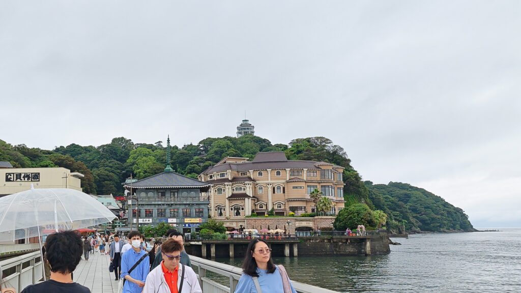 Enospa onsen on Enoshima Island - Pedestrians on a bridge with scenic views of traditional Japanese buildings and a lush hillside in the background.