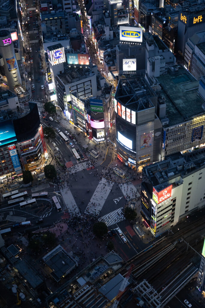 Aerial view of Shibuya Crossing at night, bustling with people and illuminated by vibrant city lights in Tokyo, Japan.