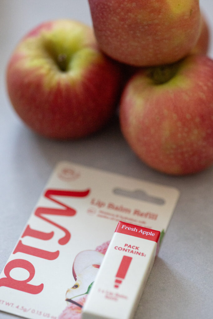 Fresh apple lip balm refill with apples in the background, emphasising natural essence and flavour.