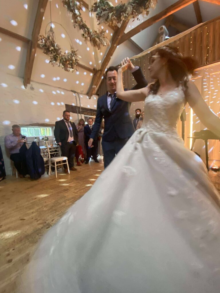 Bride and groom dancing at a rustic barn wedding, surrounded by hanging floral décor and shimmering lights.