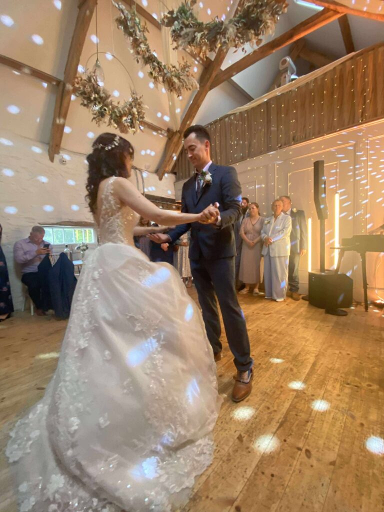 Bride and groom enjoy first dance at rustic wedding venue with wooden beams and floral decorations.