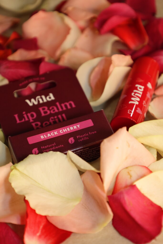 Cherry lip balm and refill surrounded by pink and white rose petals. Eco-friendly beauty product display.